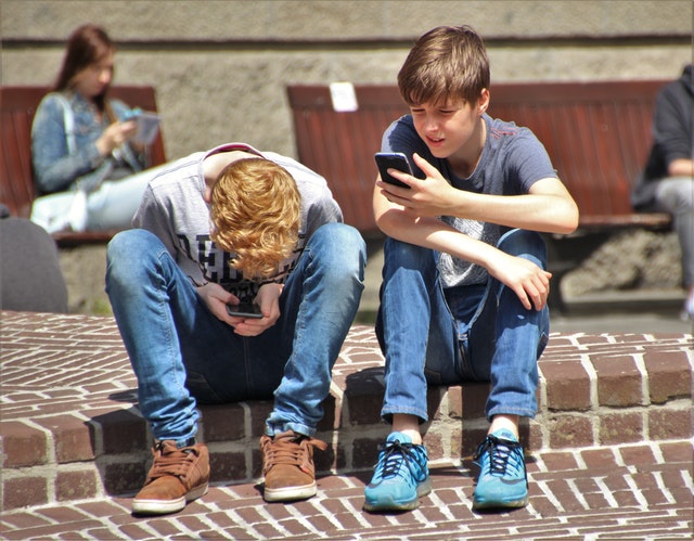 Dva kluci sedící na okraji chodníku držící v rukou mobily